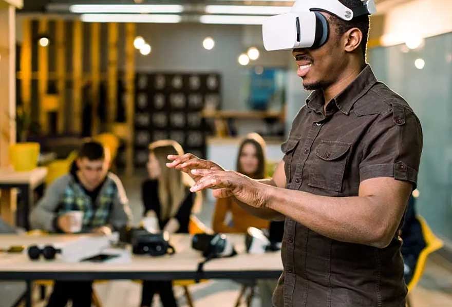 Een man draagt een VR-bril in een kantooromgeving. Op de achtergrond zitten mensen aan bureaus.