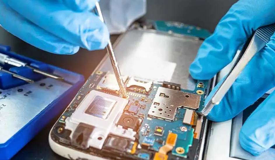 Gedemonteerde smartphone met blauwe printplaat, witte rand en kleine onderdelen. Gereedschap en blauwe handschoenen zijn zichtbaar.