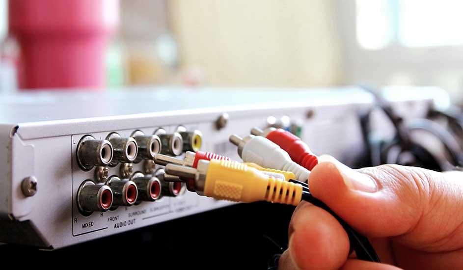 Câbles RCA rouge, blanc, jaune connectés à un appareil audio argenté. L'arrière de l'appareil comporte des ports circulaires.