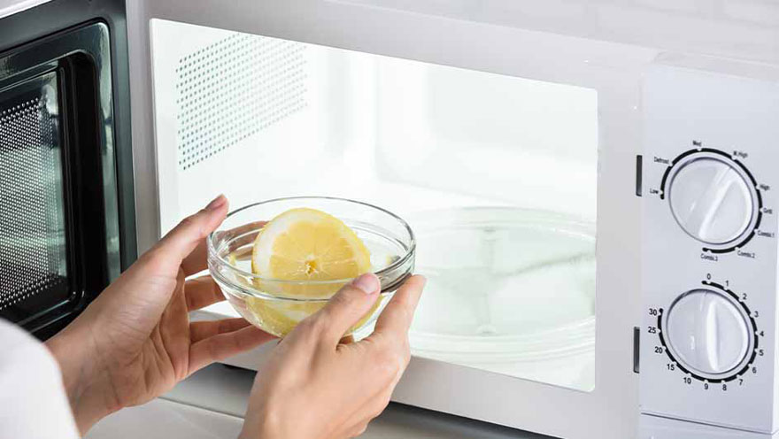 Un bol transparent avec un citron jaune est placé dans un micro-ondes blanc.