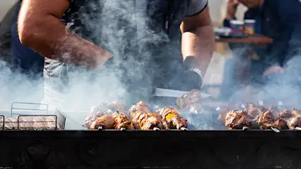 Barbecue met vlees op spiesen, omgeven door rook. Roestvrijstalen rek op de achtergrond.