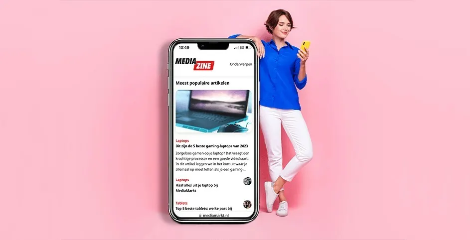 Smartphone affichant un article "Media Zine" sur fond rose uni. L'article parle de laptops et de gaming.