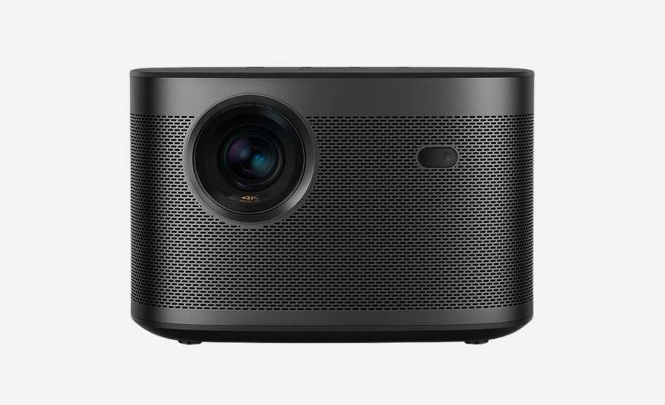 Een donkergrijze projector met een grote lens aan de linkerkant en kleine gaatjes over het hele oppervlak.