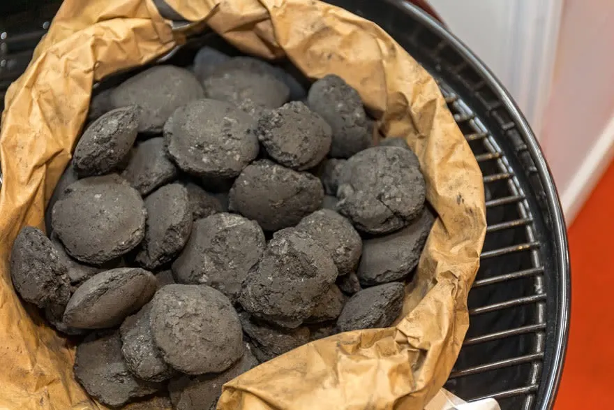 Sac de briquettes de charbon gris dans un grill noir et argenté, sur fond blanc et orange.