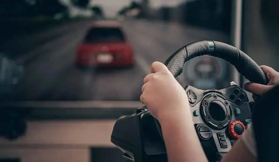 Mains tenant un volant de jeu noir avec un écran affichant une voiture rouge sur une route.