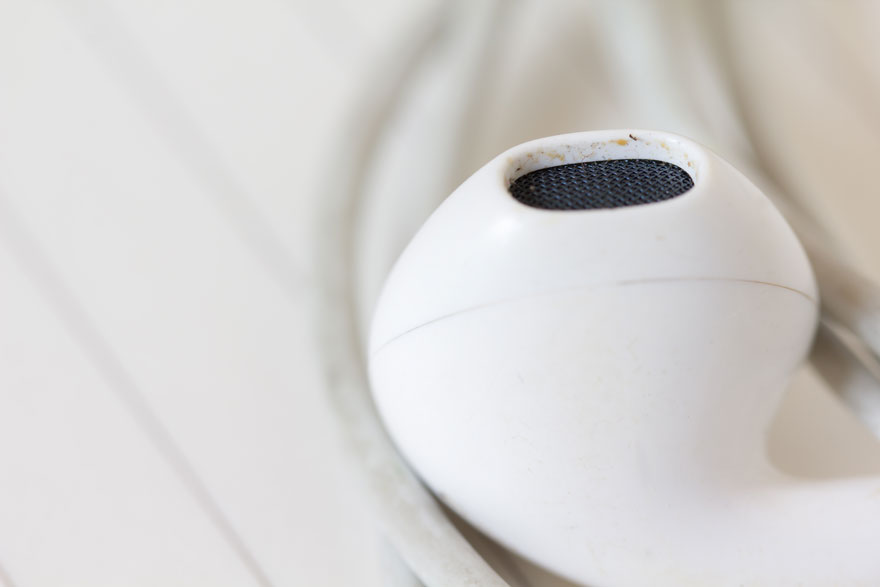 Un écouteur blanc avec l'intérieur un peu sale posé sur un tissu blanc froissé. L'image est claire et mise au point.