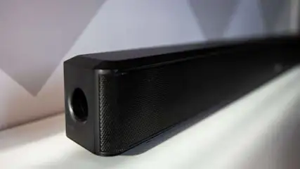 Een zwarte soundbar ligt op een witte ondergrond, met een gat aan de linkerkant en een grijze achtergrond.