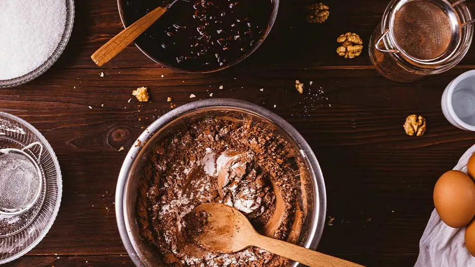 Vue de dessus d'ingrédients de pâtisserie sur une table en bois: bols de sucre, mélange au chocolat, œufs et noix.