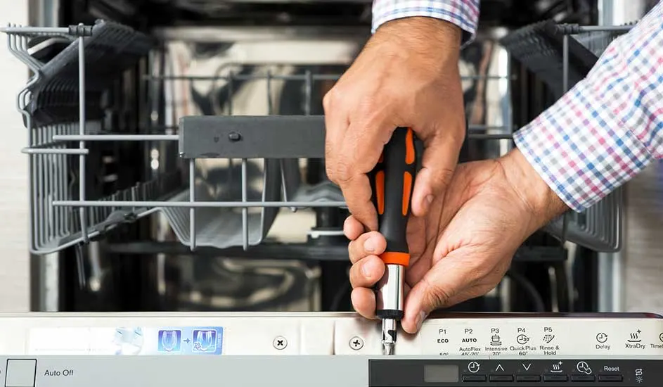 Een vaatwasser wordt gerepareerd met een oranje schroevendraaier. De vaatwasser is wit en heeft grijze rekken.