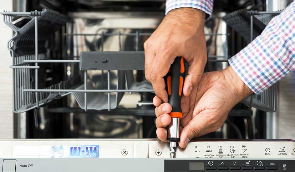 Réparation d'un lave-vaisselle. Des mains tiennent un tournevis sur le panneau de commande. L'intérieur métallique est visible.
