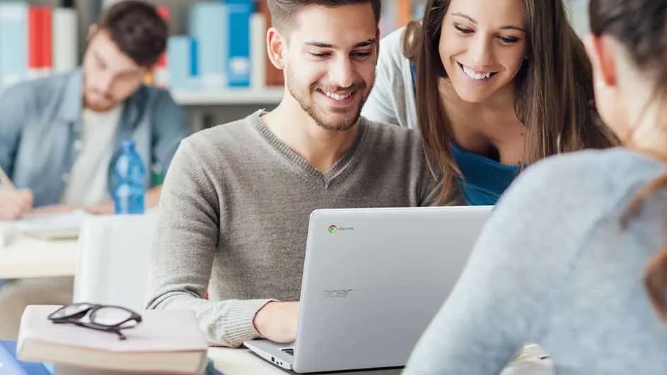 Een laptop op een bureau met boeken en een bril. Op de achtergrond staat een blauwe fles en boeken.