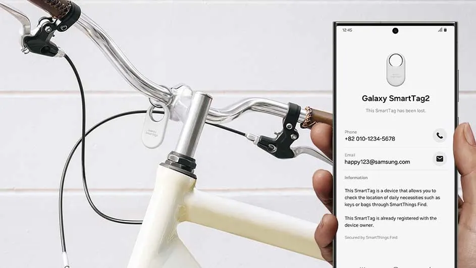 Witte fiets met zilveren stuur en een Samsung-telefoon met een SmartTag2-app in de hand.