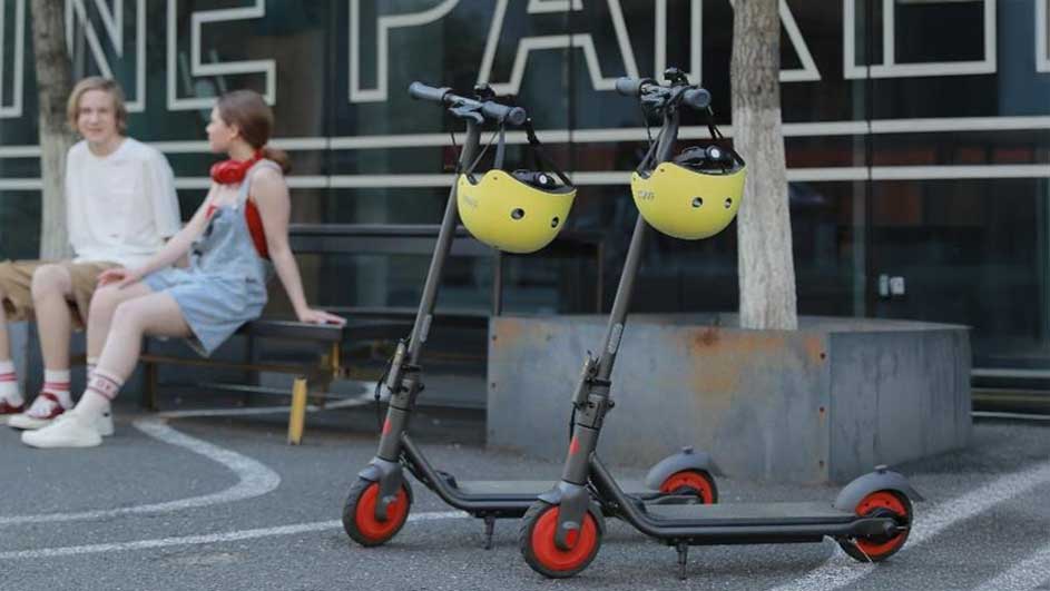 Deux trottinettes grises avec des roues orange sont garées, chacune portant un casque jaune.
