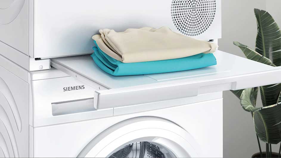 Een witte Siemens wasmachine met een uitschuifbaar rek. Op het rek liggen beige en blauwe kledingstukken.