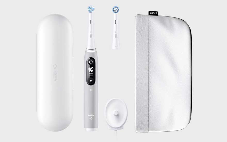 Une brosse à dents électrique noire posée debout, avec un étui blanc et deux petits accessoires à côté.