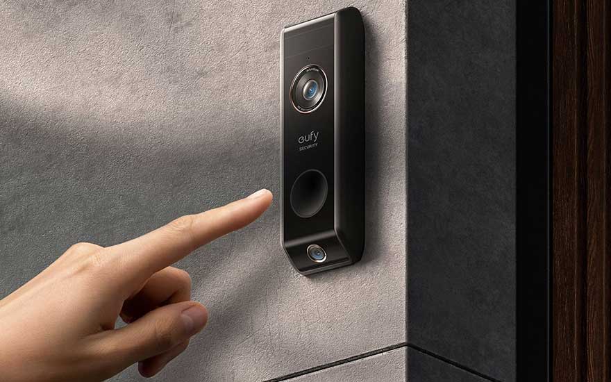 Een zwarte Eufy-deurbel aan een grijze muur, met een vinger die op de bel wijst.