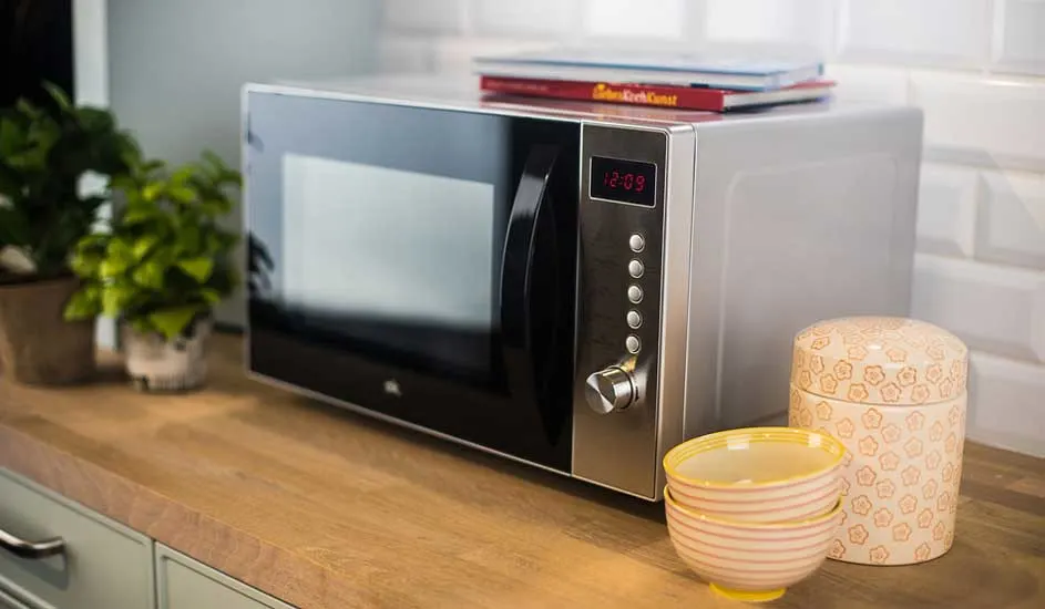 Four à micro-ondes argenté sur un comptoir en bois avec des bols, une boîte décorative, des livres et des plantes.