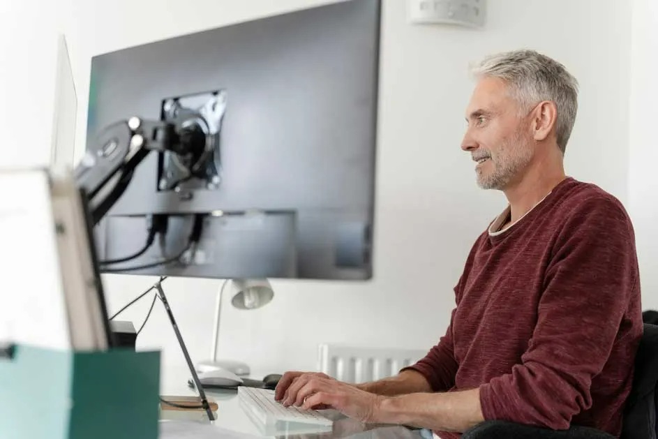Un bureau avec un grand écran d'ordinateur, un clavier, une lampe et une boîte verte sur un bureau blanc.