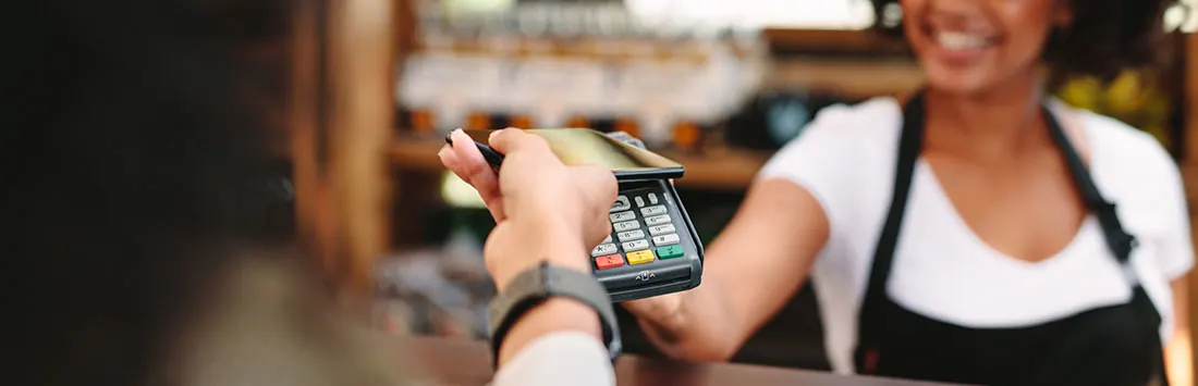 Un terminal de paiement noir est présenté pour un paiement, avec un arrière-plan flou de comptoir de café.