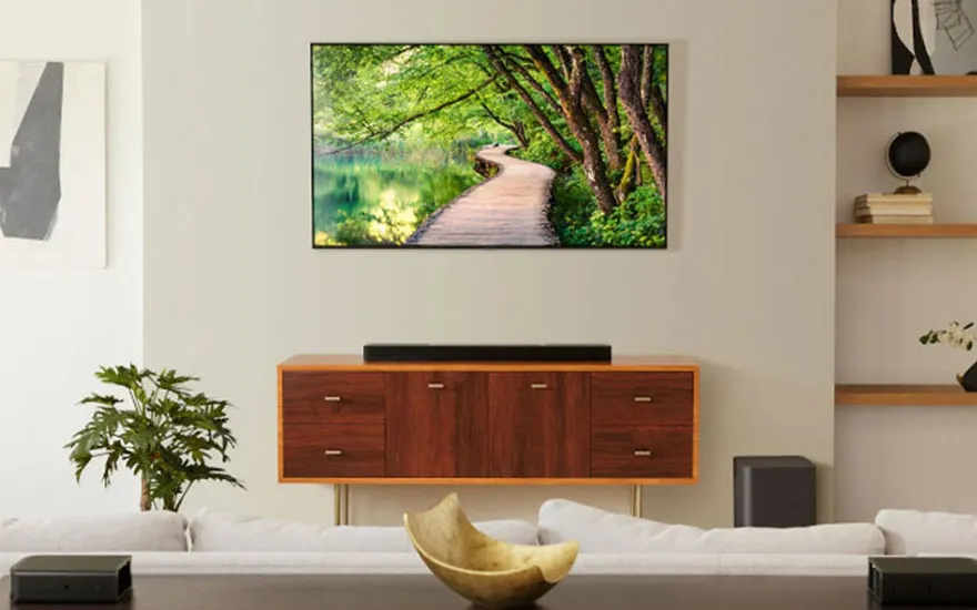 Woonkamer met houten dressoir, tv met bospad, plant, en witte sofa tegen een beige muur.