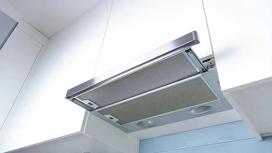 Vue rapprochée d'une hotte de cuisine argentée fixée sous une armoire blanche.