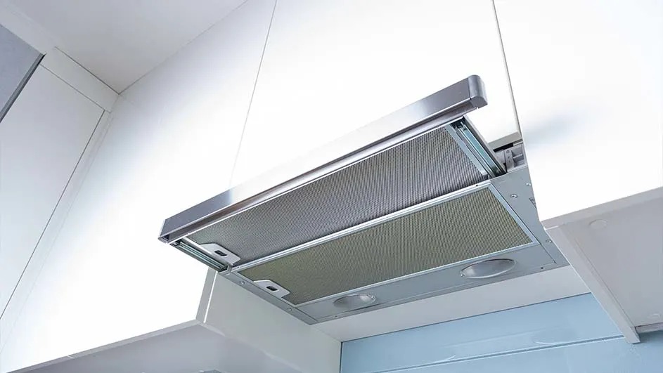 Vue rapprochée d'une hotte de cuisine argentée fixée sous une armoire blanche.