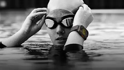 Een zwart-wit foto toont iemand in water met een zwembril en een smartwatch.