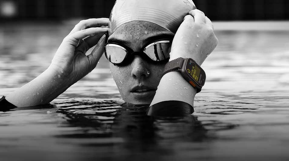 Une personne dans l'eau porte un bonnet de bain, des lunettes et une montre intelligente au poignet.