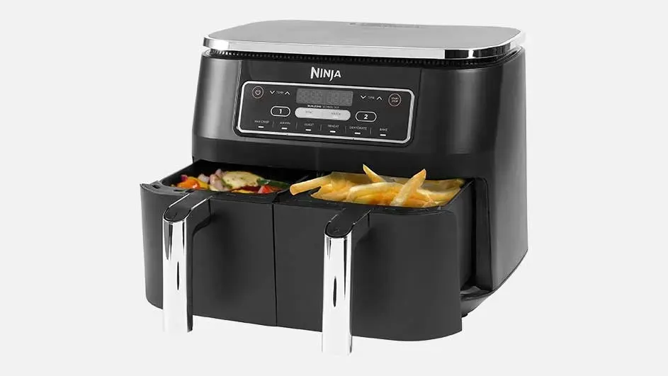 A black Ninja air fryer with two drawers, one filled with fries and the other with vegetables, is on a white background.
