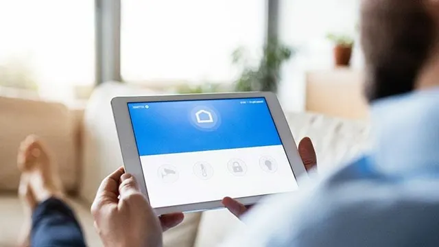 Tablette numérique blanche affichant une interface bleue et blanche avec des icônes, tenue à l'intérieur.