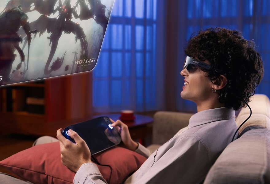 Homme sur canapé, lunettes AR, jouant sur console portable. Écran flottant affiche "Wo Long". Ambiance intérieure, lumière bleue.