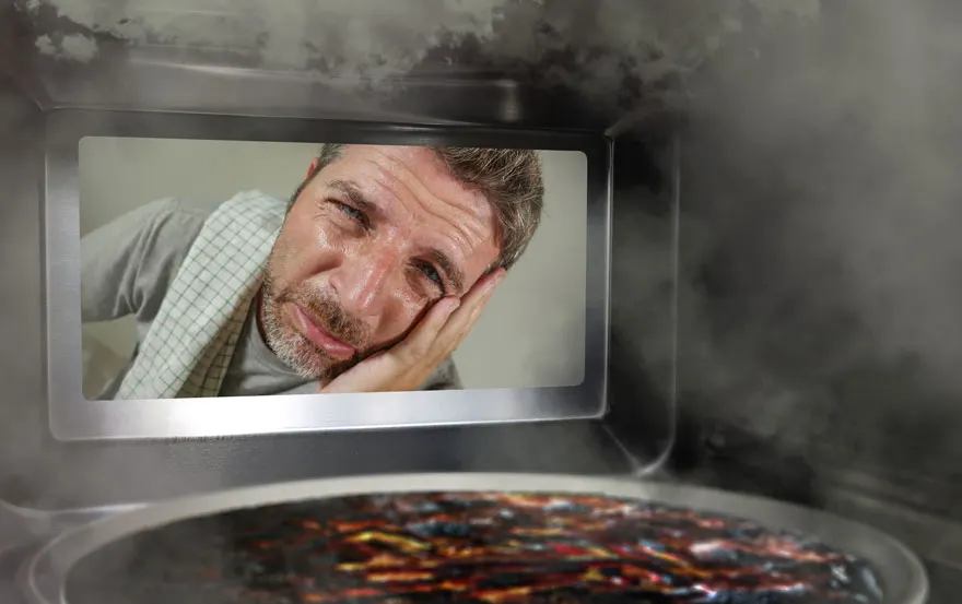 Zicht op een verbrande schotel in een oven met een man die door het raam kijkt. Er is rook.