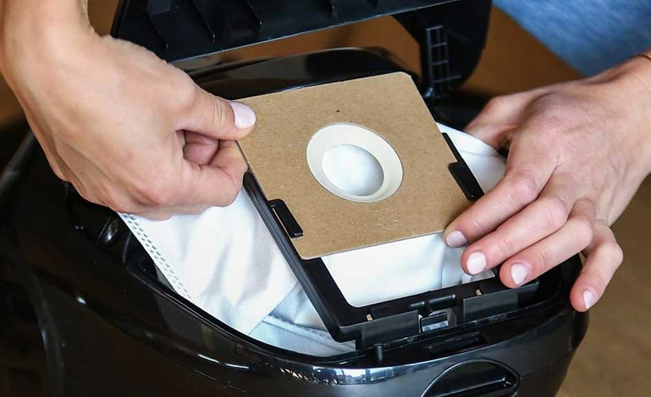 Les mains placent un sac d'aspirateur en papier brun avec un cercle blanc dans un aspirateur noir.