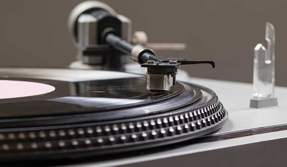 Gros plan d'une platine vinyle noire avec un disque vinyle noir et blanc, un bras de lecture noir et un stylet.