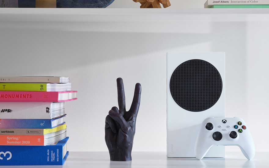 Étagère blanche avec une console Xbox blanche, une manette, une pile de livres colorés et une sculpture de main noire.