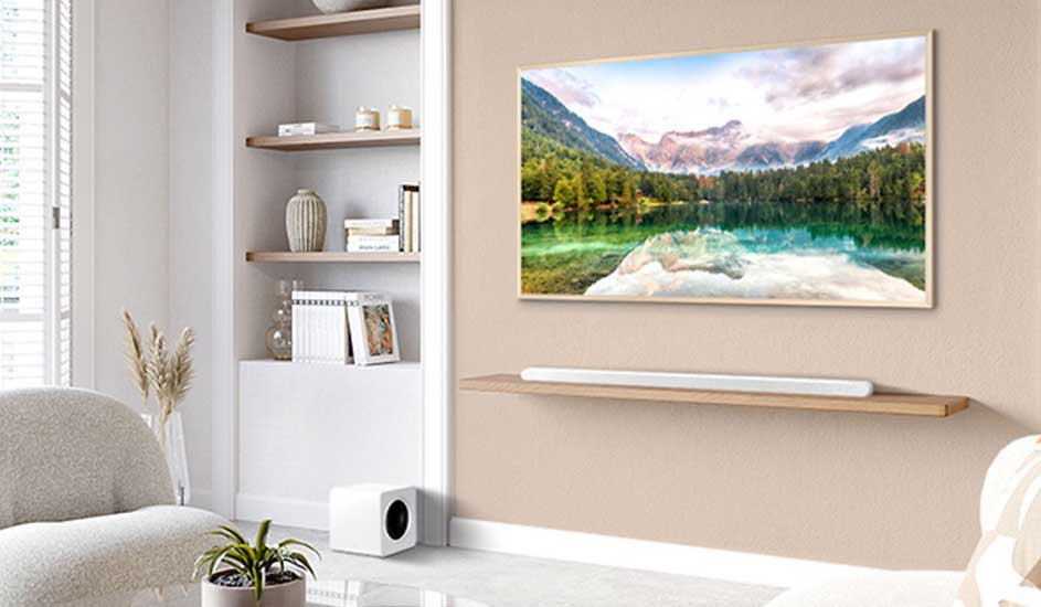 Een Samsung televisie toont een bergmeer met bomen aan de muur, daaronder een witte Samsung soundbar en subwoofer in een licht, modern interieur.