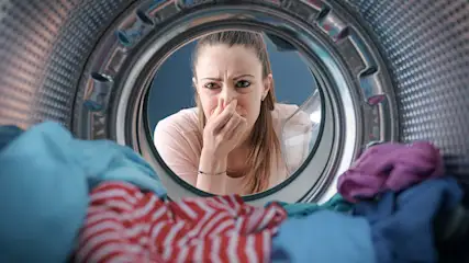 Vanuit een wasmachine: kleding in rood, blauw en paars. Achtergrond: zilveren trommel en blauwe muur.