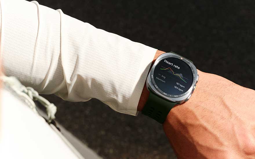 Een robuuste Galaxy Watch Ultra2 met groene band toont hartslaggegevens op een pols, buiten in fel zonlicht.