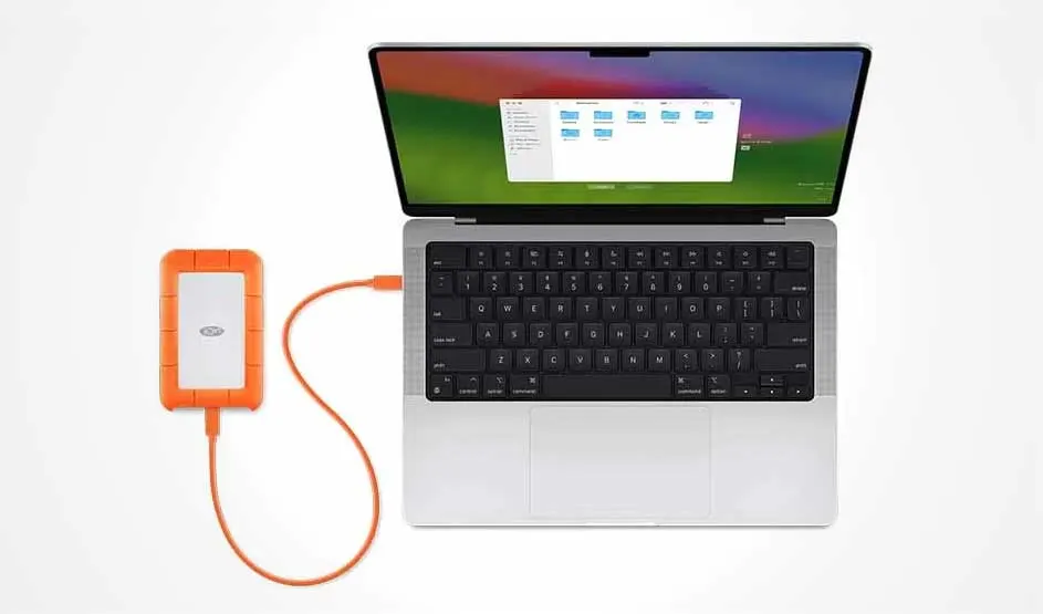 Vue du dessus d'un ordinateur portable argenté connecté à un disque dur externe orange sur fond blanc.