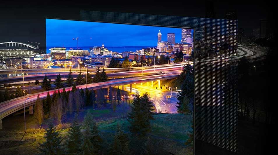 Vue nocturne de la ville avec autoroutes éclairées, bâtiments et arbres, encadrée par une structure en grille.
