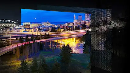 Vue nocturne de la ville avec autoroutes éclairées, bâtiments et arbres, encadrée par une structure en grille.
