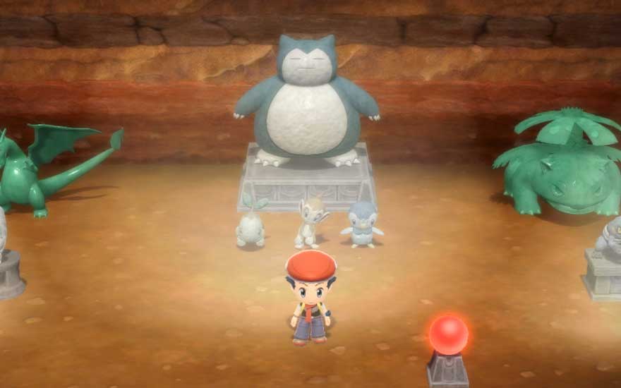 Dans une salle souterraine, un jeune dresseur se tient au milieu de statues de Pokémon, dominées par un immense Ronflex posé sur un socle central.