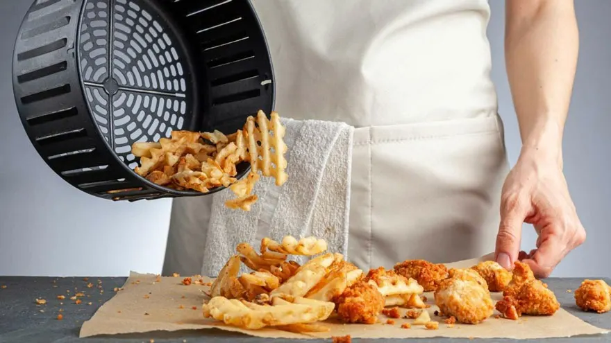 Frites et poulet sortant d'une friteuse à air, sur papier sulfurisé. Arrière-plan gris uni.