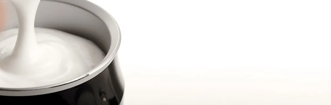 Crème blanche versée dans un pot noir et argenté sur un fond blanc uni.