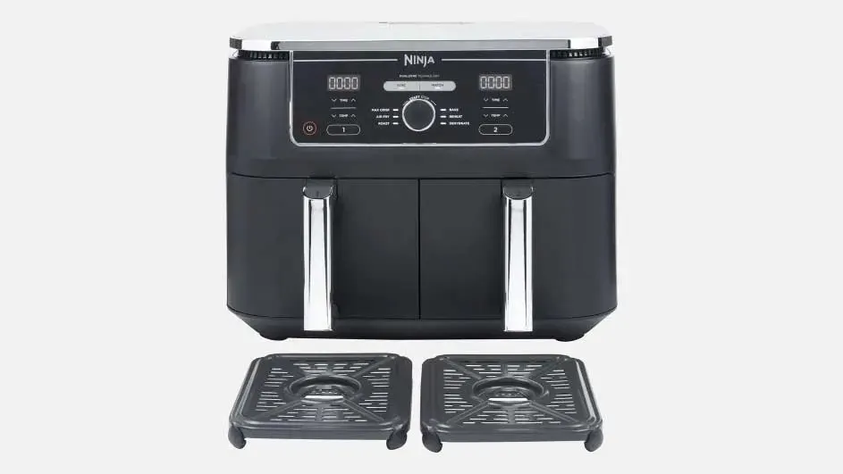 Een zwarte Ninja airfryer met twee lades en zilveren handvatten staat centraal, met twee losse grillplaten ervoor op een lichte achtergrond.