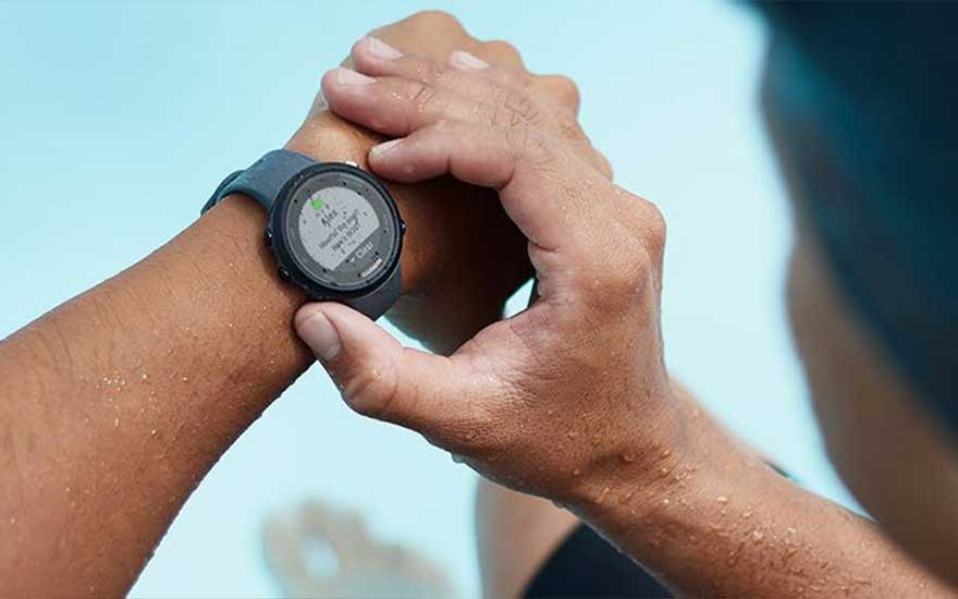 Main sur une montre connectée avec écran affichant des données, fond bleu clair.