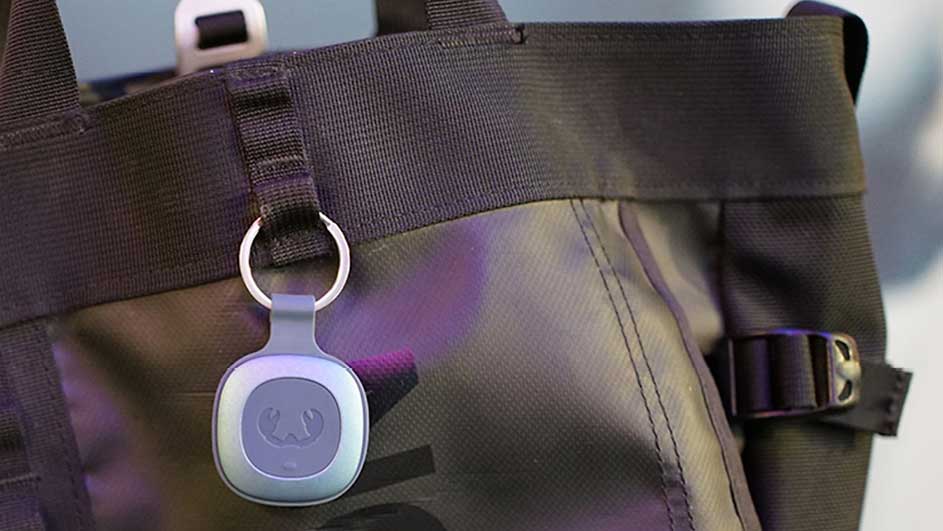 Un sac noir avec une étiquette ronde gris-bleu est suspendu à une boucle avec un anneau métallique. Une boucle est visible sur le côté.