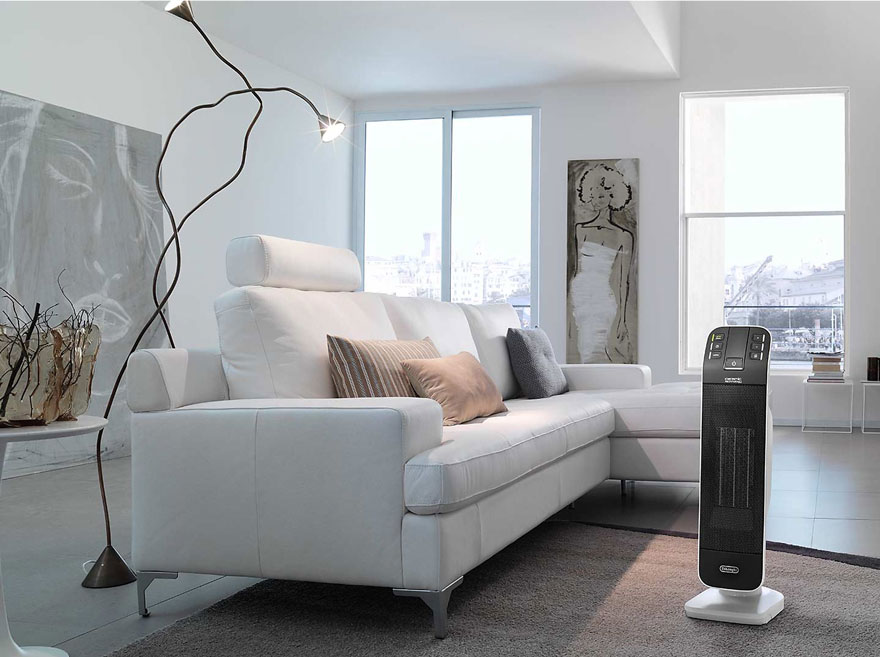 Witte hoekzetel met kussens, zwarte designlamp, schilderij, en zwarte verwarming in een lichte kamer met grote ramen. Grijze vloerbedekking.