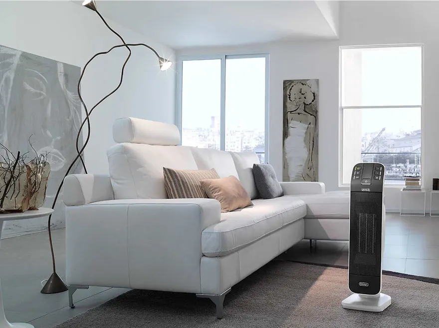 Witte hoekzetel met kussens, zwarte designlamp, schilderij, en zwarte verwarming in een lichte kamer met grote ramen. Grijze vloerbedekking.