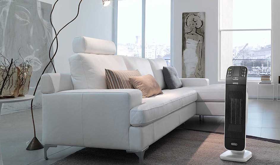 Witte hoekzetel met kussens, zwarte designlamp, schilderij, en zwarte verwarming in een lichte kamer met grote ramen. Grijze vloerbedekking.